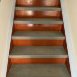 A staircase with gray steps and reddish-brown risers, bordered by light-colored walls and trim.