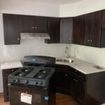 A small kitchen features dark wood cabinets, a stainless steel sink, and a black gas stove that is positioned incorrectly, facing away from the countertop.